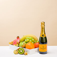 Un plateau en bois rempli de fruits délicieux accompagnés d'une petite bouteille de champagne Veuve Clicquot.