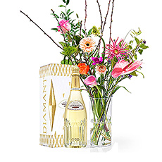 Een fles Vranken Diamant Brut champagne wordt vergezeld van een prachtig boeket met tropische, kleurrijke bloemen in een tijdloze vaas.