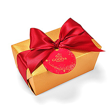 Pour la fin d'année le ballotin doré classique est décoré d'un rubon rouge vif et d'une petite carte en forme d'une boule de Noël.